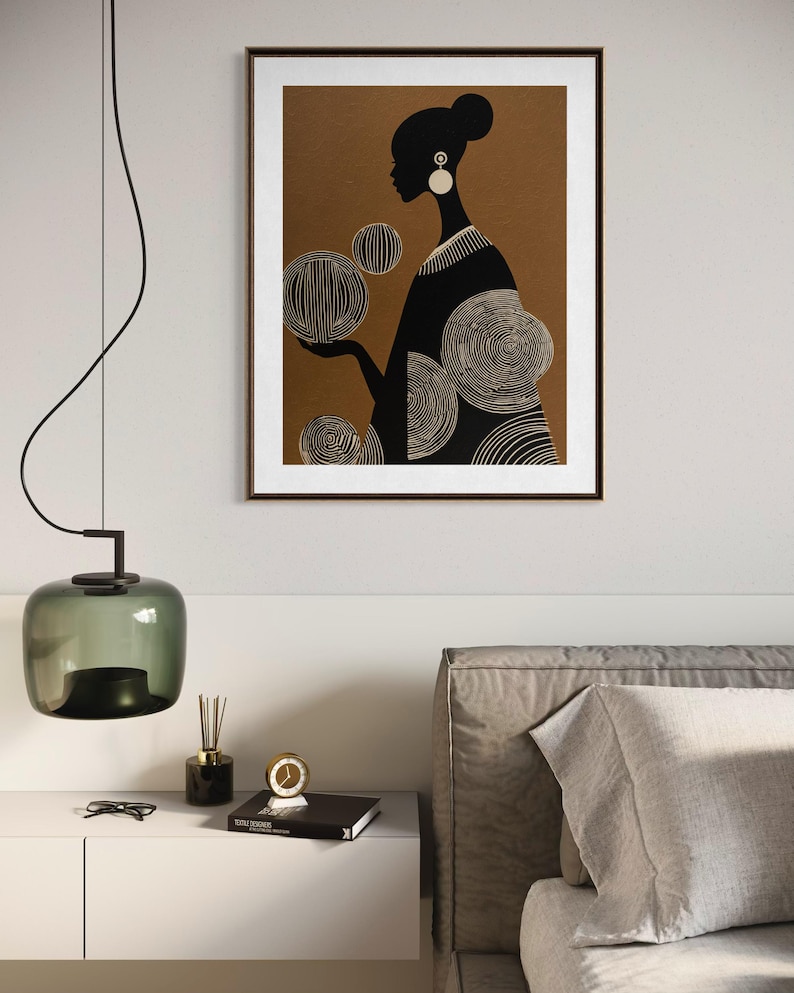 May include: A framed art print featuring a silhouette of a person with a bun, wearing earrings, and a patterned dress. The figure is set against a brown background with white circular designs. The print is in a brown frame.