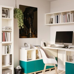 Op de afbeelding: Een moderne thuiskantoor met witte meubels, een turquoise kast en een computer. Een kunstwerk met schaakthema hangt aan de muur. Een hangplant en een zwarte prullenbak voegen decoratieve elementen toe. De kamer is goed verlicht en georganiseerd.