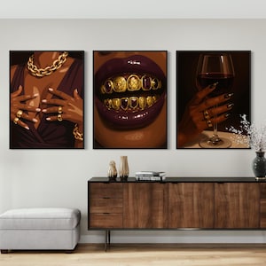 May include: Three framed art prints depicting close-ups of a person. One shows a gold chain and rings, another shows gold teeth, and the last shows a hand holding a wine glass. The art has a dark, luxurious theme.