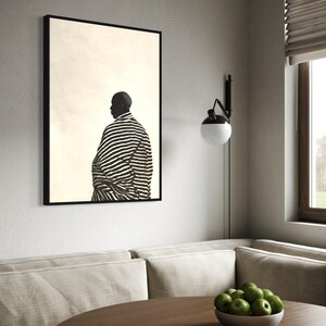 May include: A framed art print showing a black and white image of a person in a striped garment. The artwork is displayed on a white wall above a round wooden table. A bowl of green apples sits on the table.