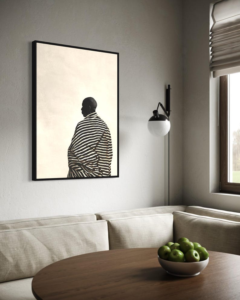 May include: A framed art print showing a black and white image of a person in a striped garment. The artwork is displayed on a white wall above a round wooden table. A bowl of green apples sits on the table.