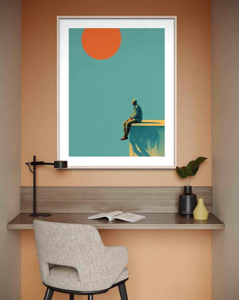 May include: Framed art print featuring a minimalist illustration of a person sitting on a ledge under a large orange sun against a teal sky. The artwork is displayed above a desk with a chair, lamp, and decorative items.