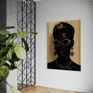 May include: A canvas art print featuring a stylized portrait of a Black person adorned with gold jewelry, including a crown, earrings, and a necklace. The person is wearing gold-rimmed sunglasses. The background is a light tan color.