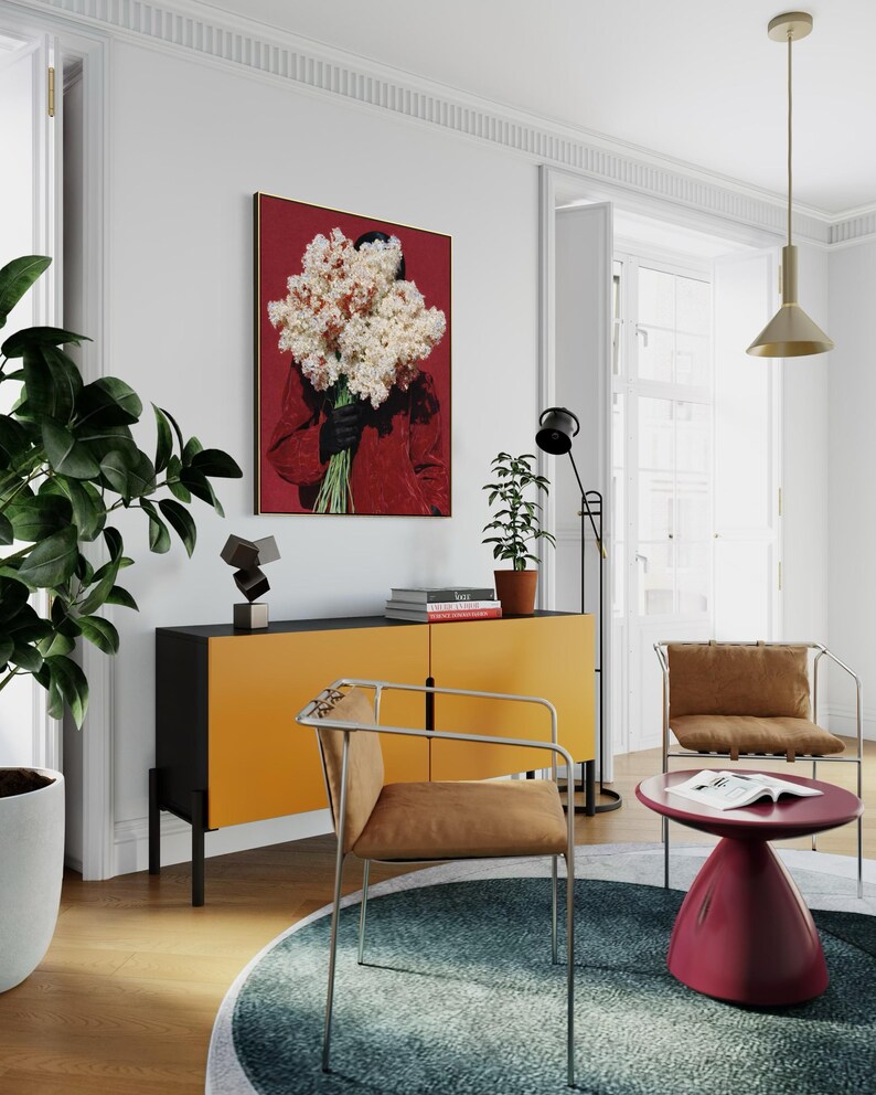 May include: An interior design scene featuring a modern living room. A large framed artwork with a red background and a person holding flowers hangs on the wall. A yellow and black cabinet, two chairs, a red side table, and a round rug complete the space.