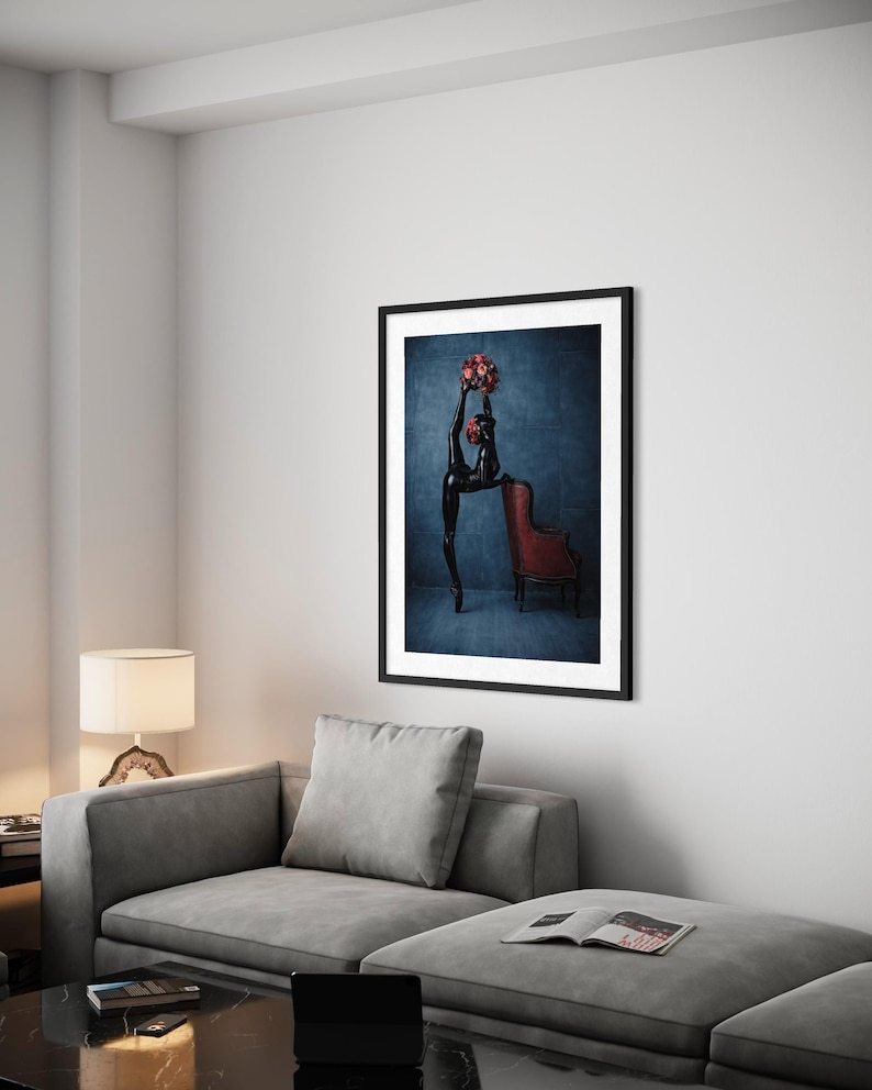 May include: A framed art print showing a black sculpture of a dancer with a bouquet of red flowers. The dancer is positioned in front of a red armchair against a dark blue background. The artwork is displayed in a modern living room.