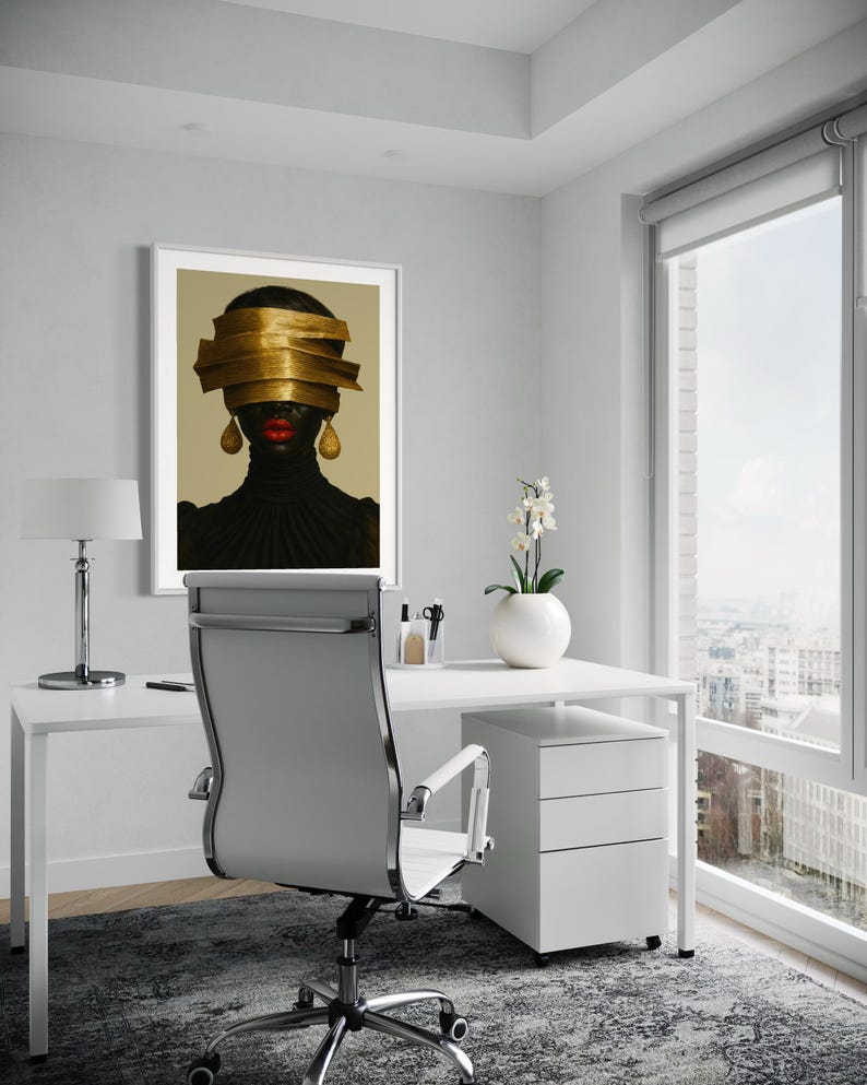 May include: An office setting with a white desk, chair, and a framed artwork. The artwork features a portrait of a person with gold headwear and red lips. A white lamp and a vase with flowers are also visible.