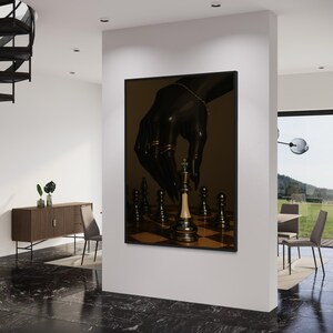 Op de afbeelding: Een ingelijste kunstdruk met een schaakspel. Een zwarte hand met gouden ringen en een armband zweeft boven het schaakbord, klaar om de witte koning te verplaatsen. Het kunstwerk heeft een donkere, dramatische esthetiek.