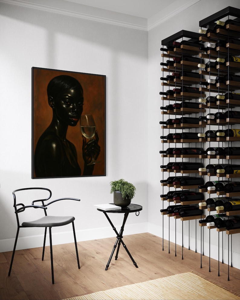 May include: A modern wine room featuring a black metal wine rack filled with bottles. A framed portrait hangs on the wall, and a small black table with a plant and chair are in the foreground. The room has a minimalist design with light-colored walls and hardwood floors.