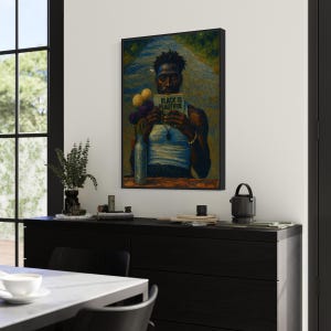 Puede incluir: Una obra de arte enmarcada que presenta un retrato de una persona negra sosteniendo un libro con el texto "BLACK IS BEAUTIFUL". La obra de arte se exhibe en una pared sobre un mueble negro. Un jarr&oacute;n con flores y otros objetos decorativos est&aacute;n en el mueble.