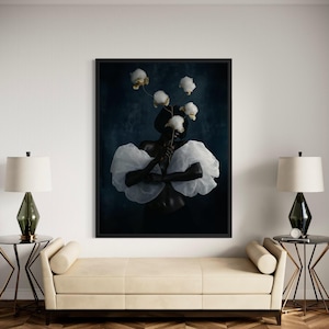 May include: A framed art print featuring a person adorned with white, cloud-like fabric and holding white flowers. The artwork has a dark blue background and is displayed above a cream-colored bench with two side tables and lamps.