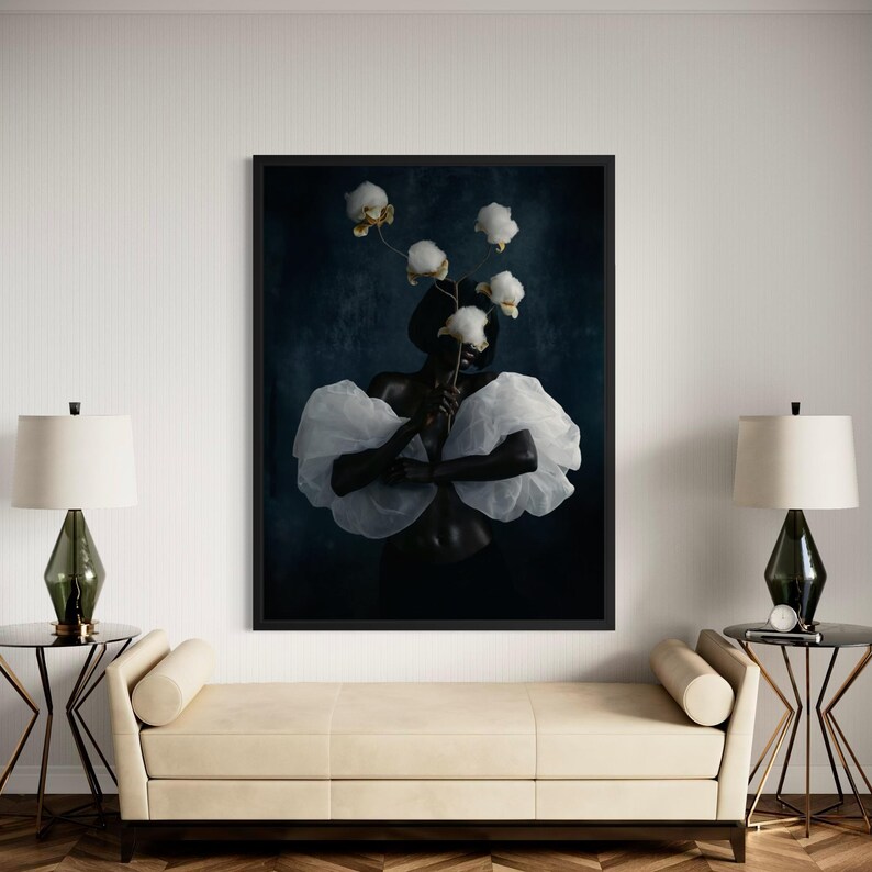 May include: A framed art print featuring a person adorned with white, cloud-like fabric and holding white flowers. The artwork has a dark blue background and is displayed above a cream-colored bench with two side tables and lamps.