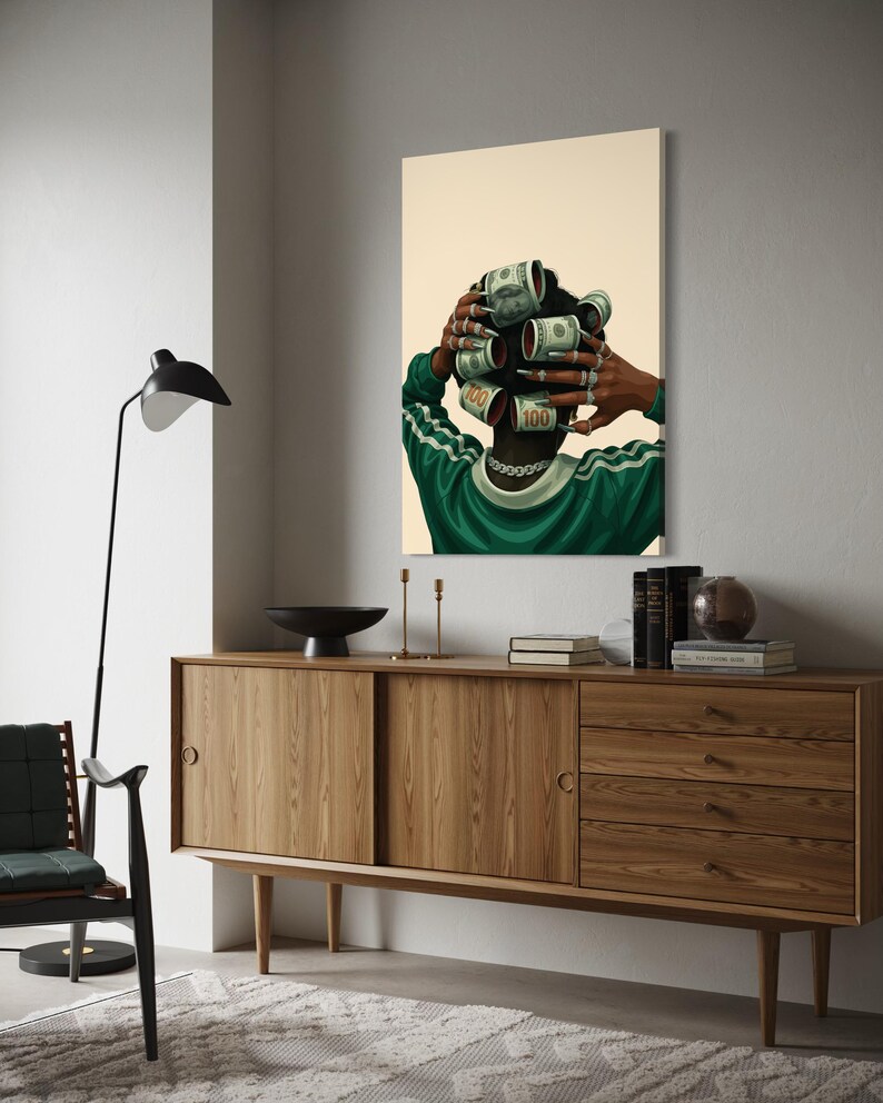 May include: A framed art print depicts a person with dollar bills rolled into curlers. The person wears a green and white striped shirt and a silver chain. The artwork hangs above a wooden cabinet with a black bowl and candles.