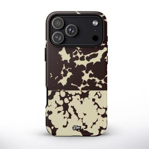 Op de afbeelding: Een telefoonhoesje met een bruin en crèmekleurig koeienhuidpatroon. De hoes heeft een zwart cameramodule met drie lenzen. De onderste helft van de hoes heeft een crèmekleurige achtergrond met bruine vlekken. De tekst "Casual Craft" staat onderaan.