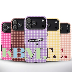 May include: Five phone cases with a gingham design in pink, brown, purple, yellow, and peach. Each case features a different initial in a contrasting colour. The purple case has a "CUSTOM MADE" sticker.