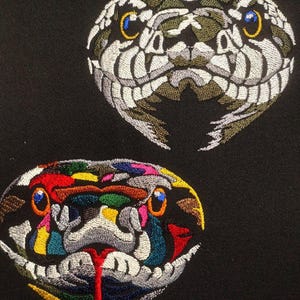 以下が含まれることがあります： 黒い生地に刺繍された2つのヘビの頭のパッチ。1つは緑、白、茶色の色合いで、青と黄色の目があります。もう1つは、赤、黄、青、ピンクなどの鮮やかな色の組み合わせで、オレンジ色の目と赤い舌があります。