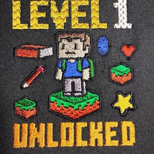 May include: Embroidered patch with a pixelated video game theme. The design features the text "LEVEL 1 UNLOCKED" in yellow, a pixelated character, and various game elements like a heart, star, and floating island, all on a black background.