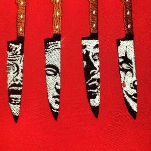 May include: Four embroidered knives with black and white designs on a red fabric background.