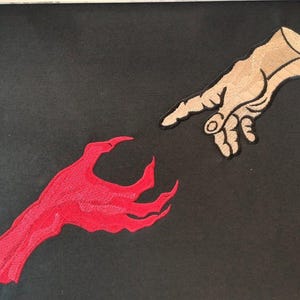 May include: A red hand reaches out to touch a beige hand, both hands are stylized and appear to be embroidered on a black fabric.