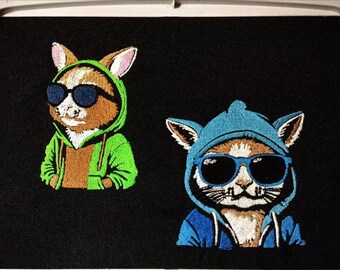 May include: Two embroidered patches of animals wearing sunglasses and hoodies. The first patch is a green hoodie with a brown rabbit wearing black sunglasses. The second patch is a blue hoodie with a white cat wearing blue sunglasses.