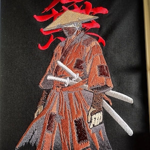 Op de afbeelding: Een geborduurde patch op zwarte stof met een krijger die een beige conische hoed en een gehavend oranje gewaad draagt. De figuur draagt twee witte zwaarden aan de taille. Achter de krijger is een groot rood Japans kanji-teken geborduurd.