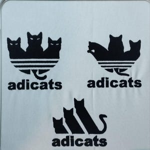 May include: Three black cat silhouettes in a triangle shape with the word "adicats" below. The same design is repeated twice, once with the cats facing forward and once with the cats facing backward. The third design features three cats in a row with the word "adicats" below.