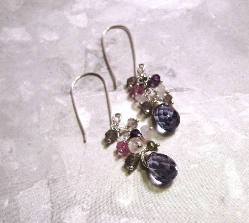 May include: A pair of silver dangle earrings with a cluster of purple, pink, and white gemstones. The earrings feature a teardrop-shaped purple gemstone at the bottom.