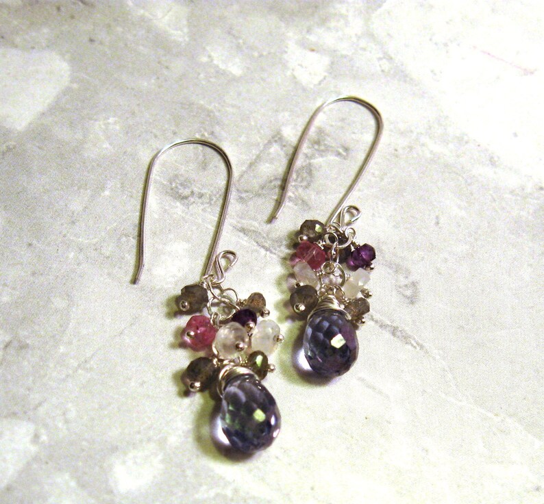 May include: A pair of silver dangle earrings with a cluster of colorful gemstones, including pink, purple, and white, and a larger blue gemstone at the bottom.