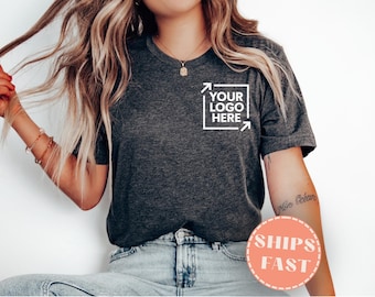 May include: Charcoal grey t-shirt featuring a white square logo with the text "YOUR LOGO HERE". The shirt is worn with blue jeans. A round sticker with the words "SHIPS FAST" is also visible in the image.