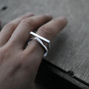 May include: A silver ring with a geometric design. The ring is made of three interlocking pieces, each with a different shape. The ring is worn on a finger.