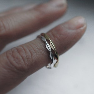 May include: A close-up of a finger wearing two braided rings, one silver and one gold.