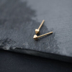 May include: A pair of gold-toned stud earrings with a geometric, pyramid-shaped design.