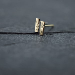 May include: A pair of gold bar stud earrings with a leaf design.