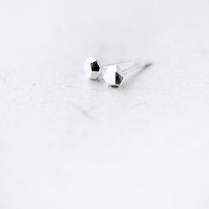May include: A pair of silver geometric stud earrings. The earrings are small and have a faceted design.