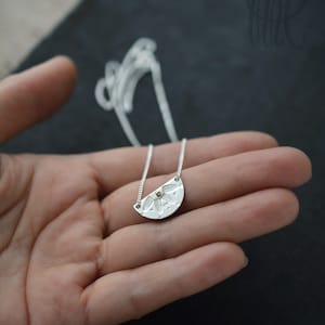 May include: A silver necklace with a half-circle pendant featuring a detailed floral design and a small gold accent.
