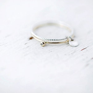 May include: Two delicate rings, one silver and one gold, are stacked on a white surface. The gold ring has a small diamond set in the centre.
