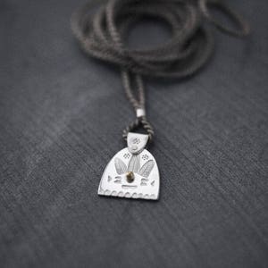 May include: A silver pendant necklace featuring a detailed design of leaves and a small gold dot at the centre. The pendant is attached to a grey cord.