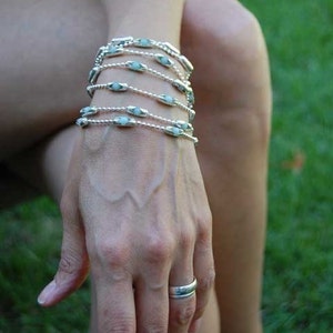 May include: A woman's wrist adorned with multiple silver bracelets featuring light blue oval-shaped beads. A silver ring is worn on the ring finger of her right hand.