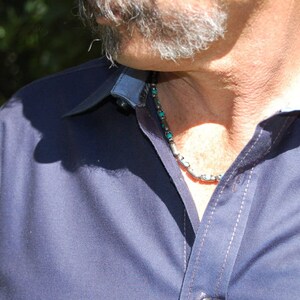 May include: A close-up of a navy blue button-down shirt with a contrasting light blue collar and cuffs. The shirt has white stitching and is paired with a silver and turquoise beaded necklace. The image is taken outdoors.