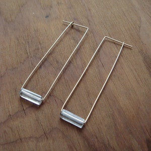 May include: A pair of gold earrings with clear glass rectangular bars hanging from the bottom.