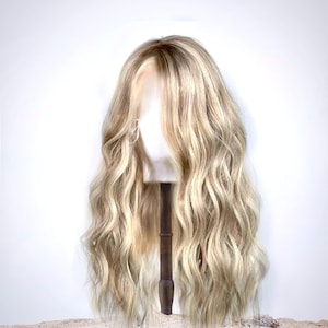 Peut inclure: Une longue perruque blonde ondulée avec des mèches. La perruque est sur une tête de mannequin et est coiffée en vagues lâches.