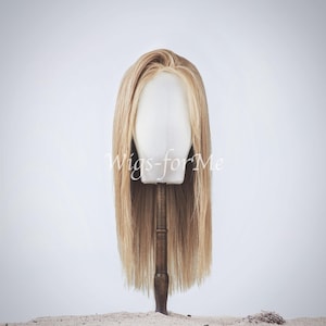 Peut inclure: Une perruque longue, droite et blonde clair sur une tête de mannequin. La perruque est coiffée d'une raie au milieu et a un aspect naturel et fluide.