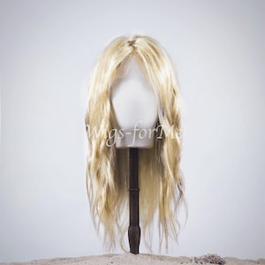 May include: A blonde wig with long, wavy hair is displayed on a mannequin head. The wig is styled with loose waves and a natural-looking part. The mannequin head is mounted on a wooden stand, set against a white background. The text "Wigs-forMe" is visible.