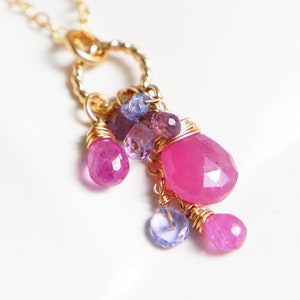 Peut inclure: Un collier en chaîne dorée avec un pendentif en pierres précieuses roses et violettes. Le pendentif présente une grande pierre précieuse rose entourée de plus petites pierres précieuses roses et violettes.