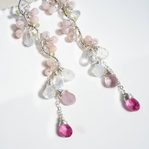 May include: Elegant silver earrings with a floral design. The earrings feature clusters of pink and white beads, with dangling teardrop-shaped pink gemstones. The design incorporates small green beads and clear, faceted stones.