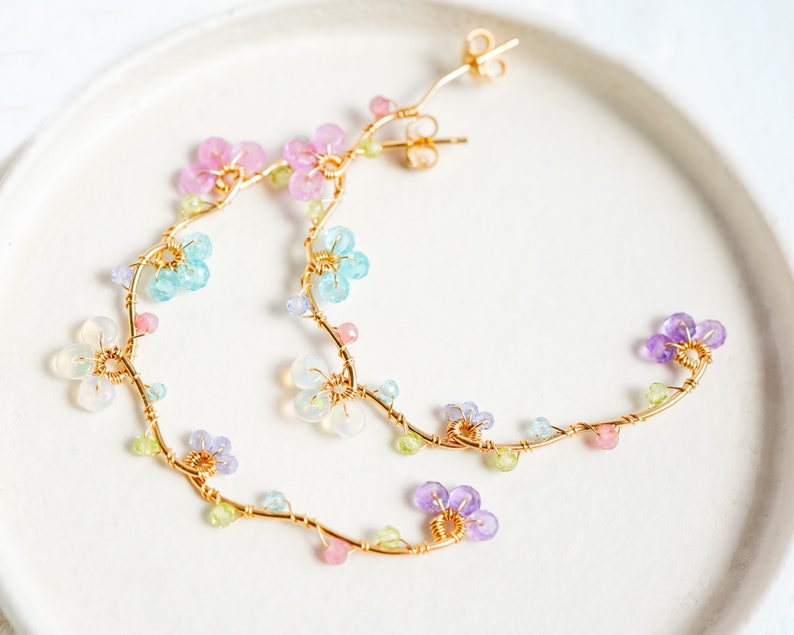 Pastel color gemstone beads such as topaz, opal, tanzanite and amethyst.. are formed into small flowers on vine hoop.