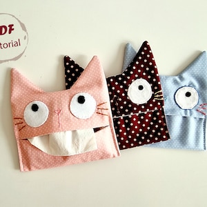 May include: Three cat-shaped tissue box covers. The covers are made of fabric with polka dots. The pink cover has a white tissue inside. The brown cover has white polka dots on a dark brown background. The blue cover has white polka dots on a light blue background.