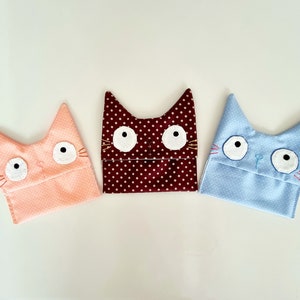 May include: Three fabric cat-shaped pouches with embroidered eyes and whiskers. The pouches are pink with white polka dots, brown with white polka dots, and light blue with white polka dots.
