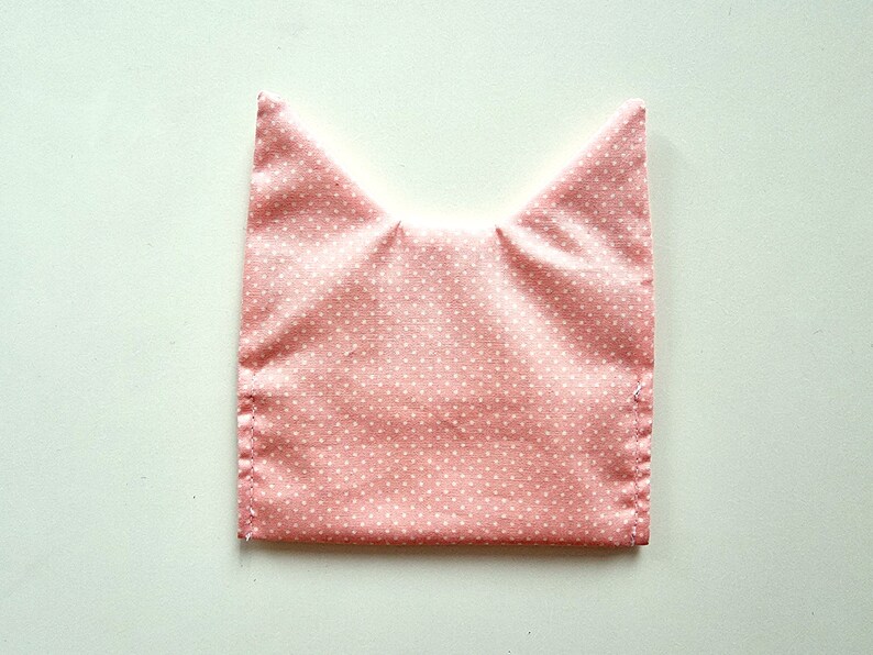 May include: Pink fabric with white polka dots sewn into a cat ear shape.