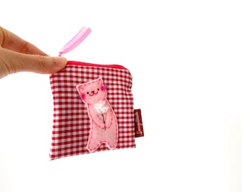 May include: A small square zippered pouch made of red and white gingham fabric. A light pink felt cat appliqué holding a small white flower is stitched onto the front. A pink ribbon is attached to the zipper pull, and a small brown brand tag is visible.