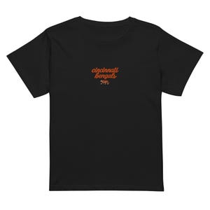 Op de afbeelding: Een zwart t-shirt met korte mouwen en de tekst cincinnati bengals in oranje cursief schrift in het midden op de borst, geplaatst boven een kleine, gedetailleerde afbeelding van een lopende tijger in de kleuren oranje, zwart en wit.